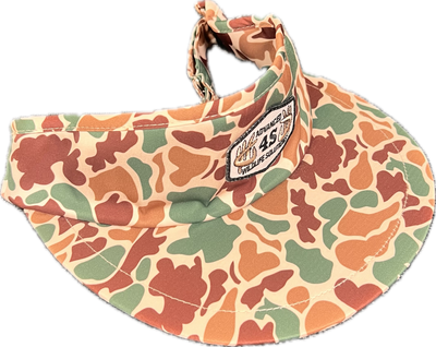 A camo print visor with an adjustable buckle in the back and a white hexagon patch on the front.